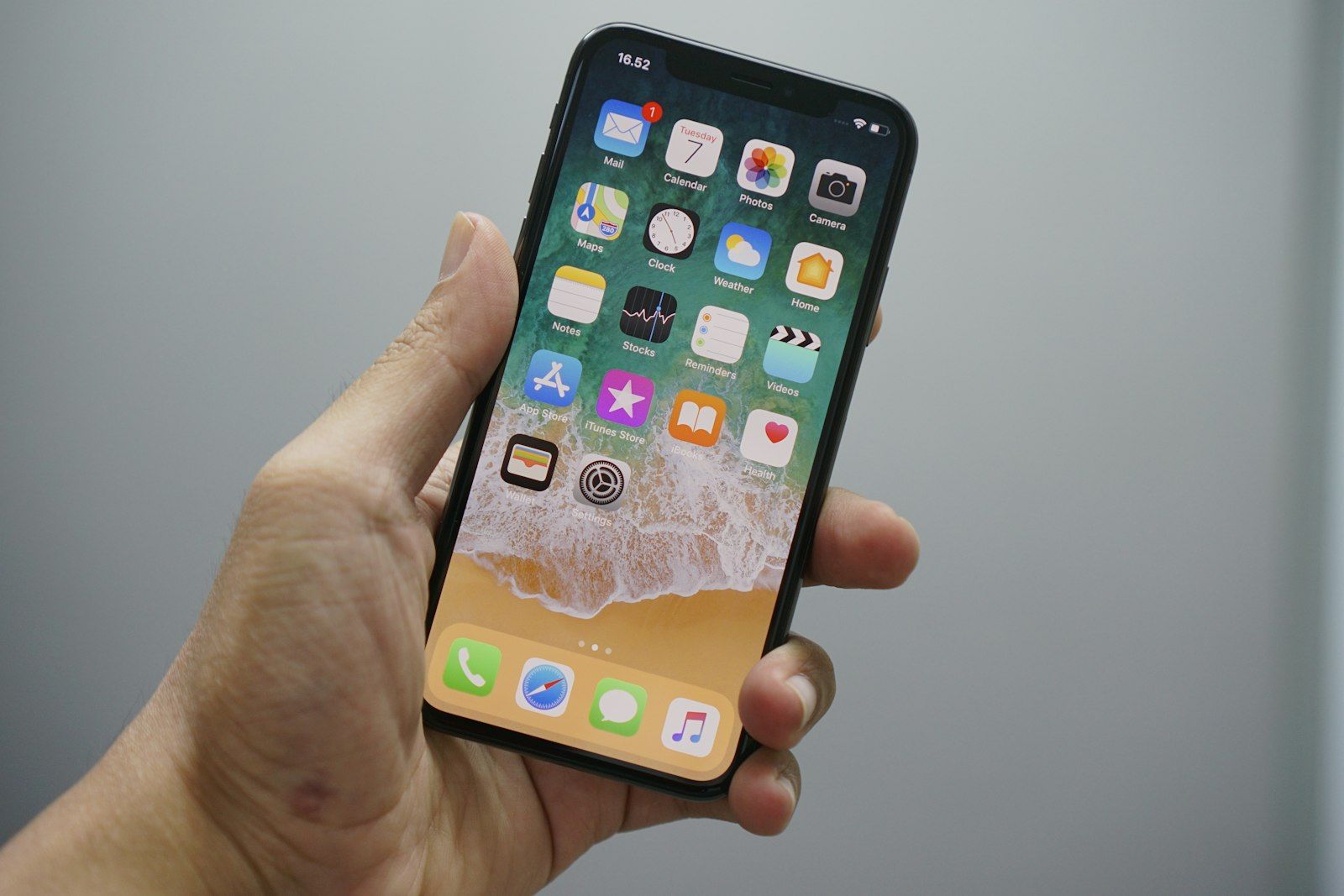 Hand holding an iPhone showing the iOS home screen