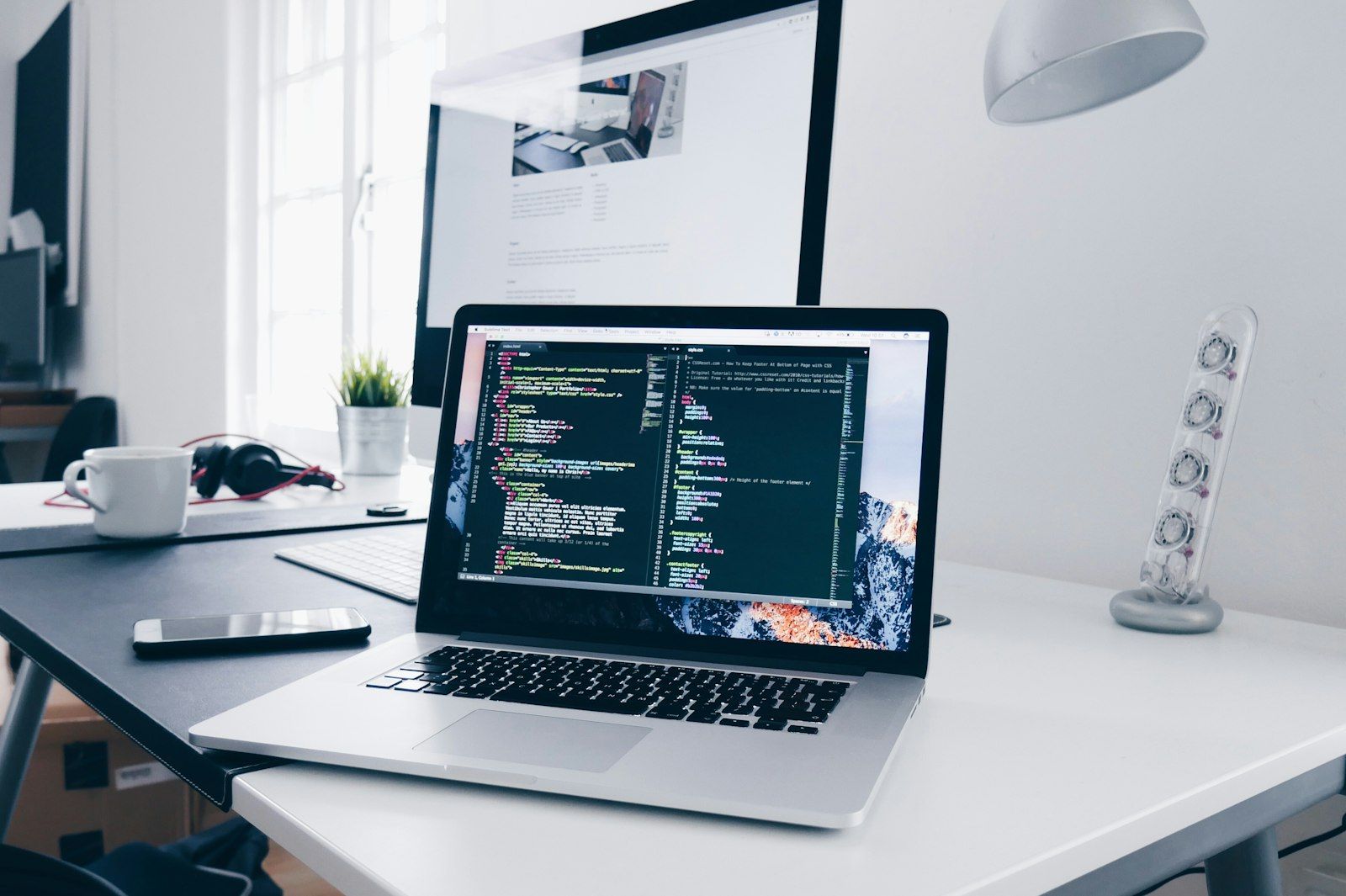 Laptop and desktop computer on a bright desk with headphones and coffee